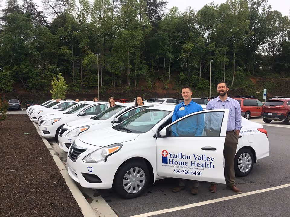 Line of white company cars in a parking lot with staff posing beside them.