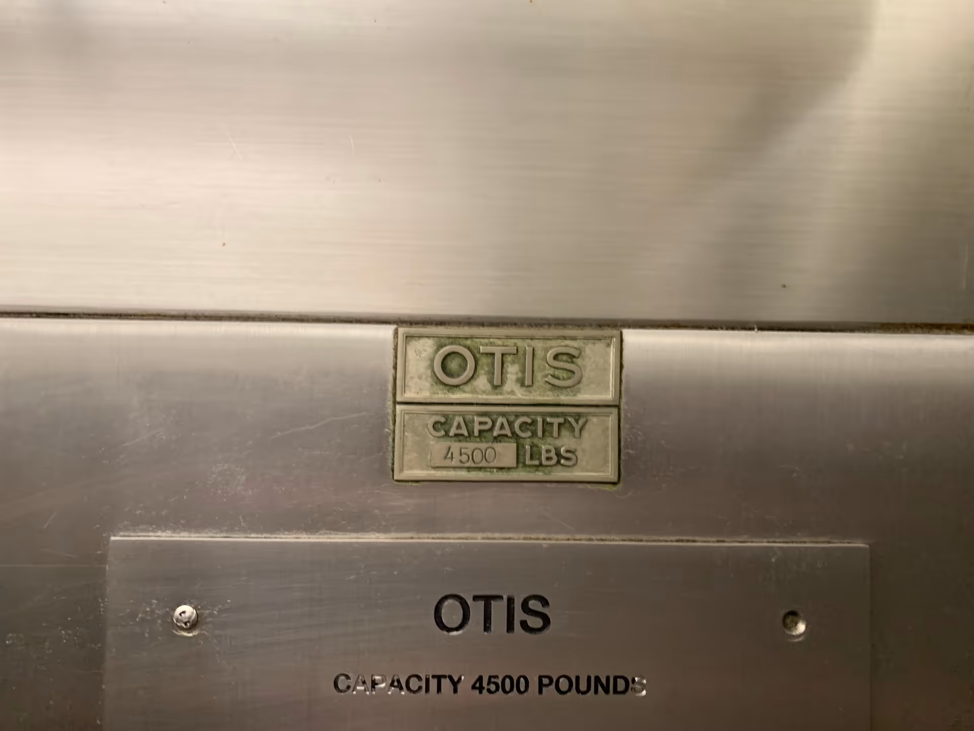 Close-up of an Otis elevator plaque and capacity label on stainless steel wall
