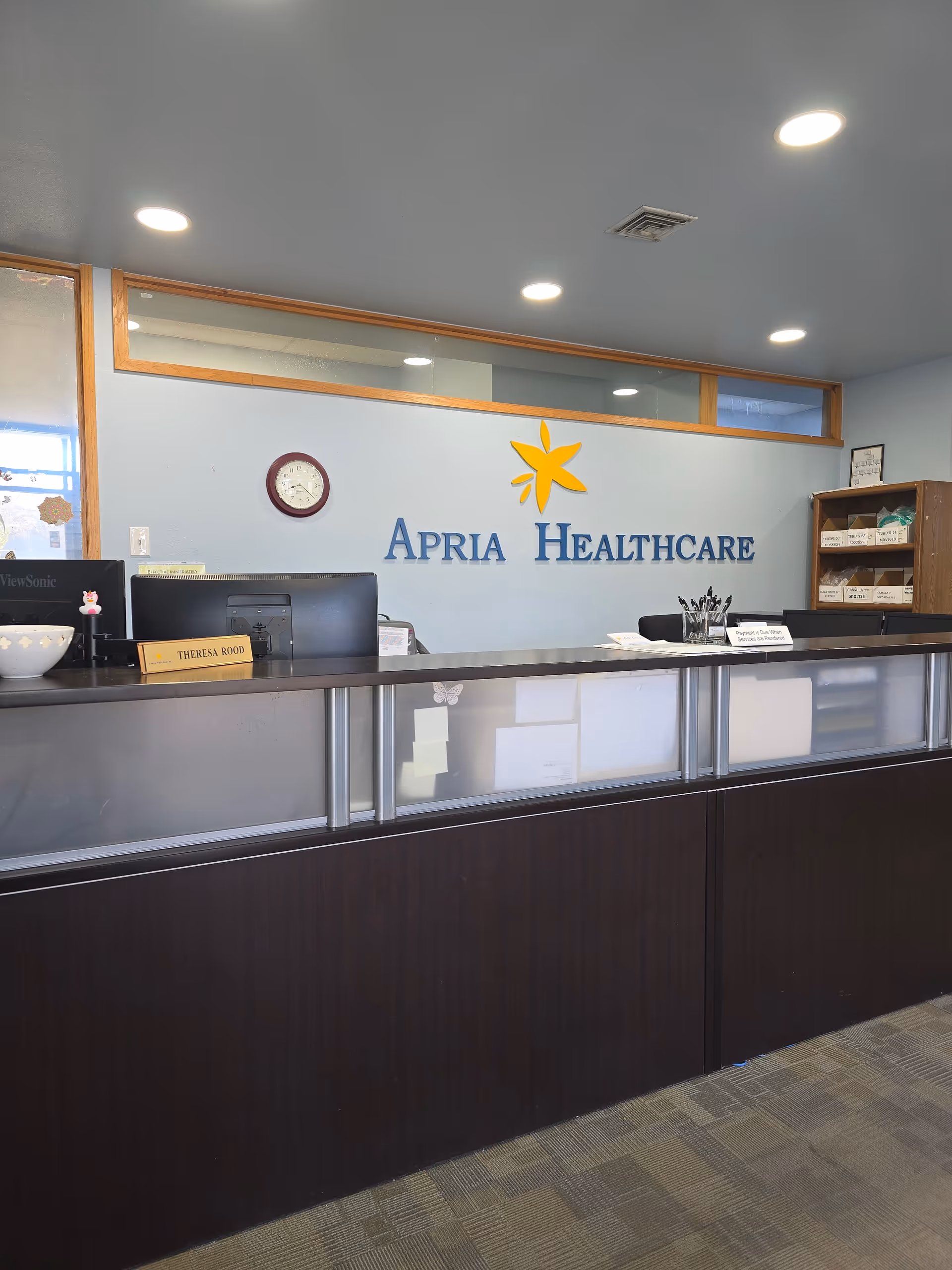 Reception desk in Apria Healthcare lobby with blue logo wall behind it.