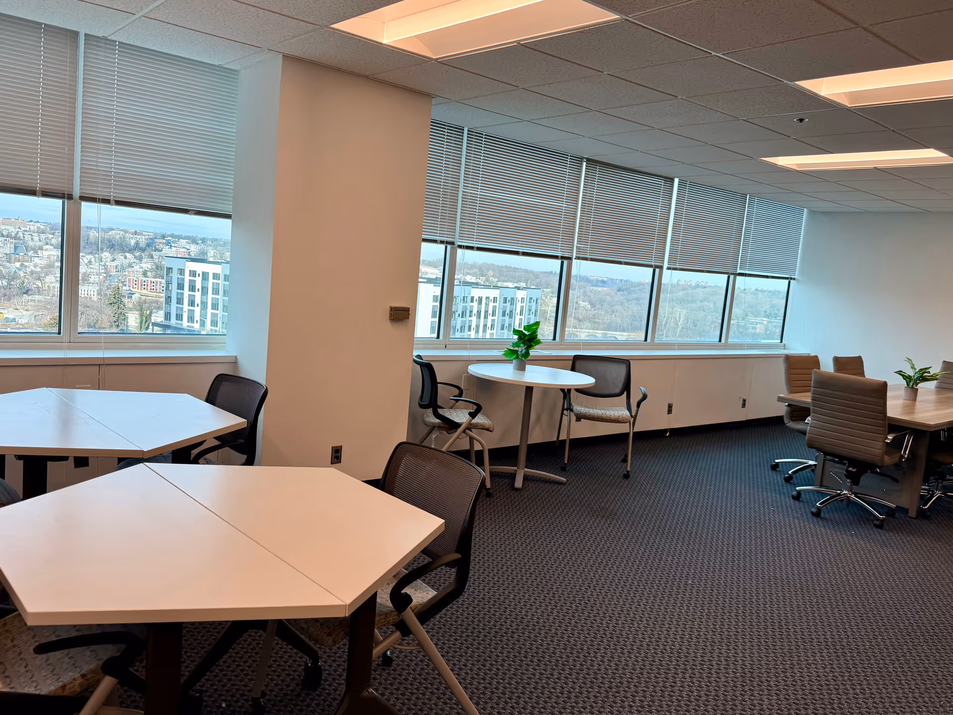 Modern interior with tables and chairs by large windows overlooking the city.