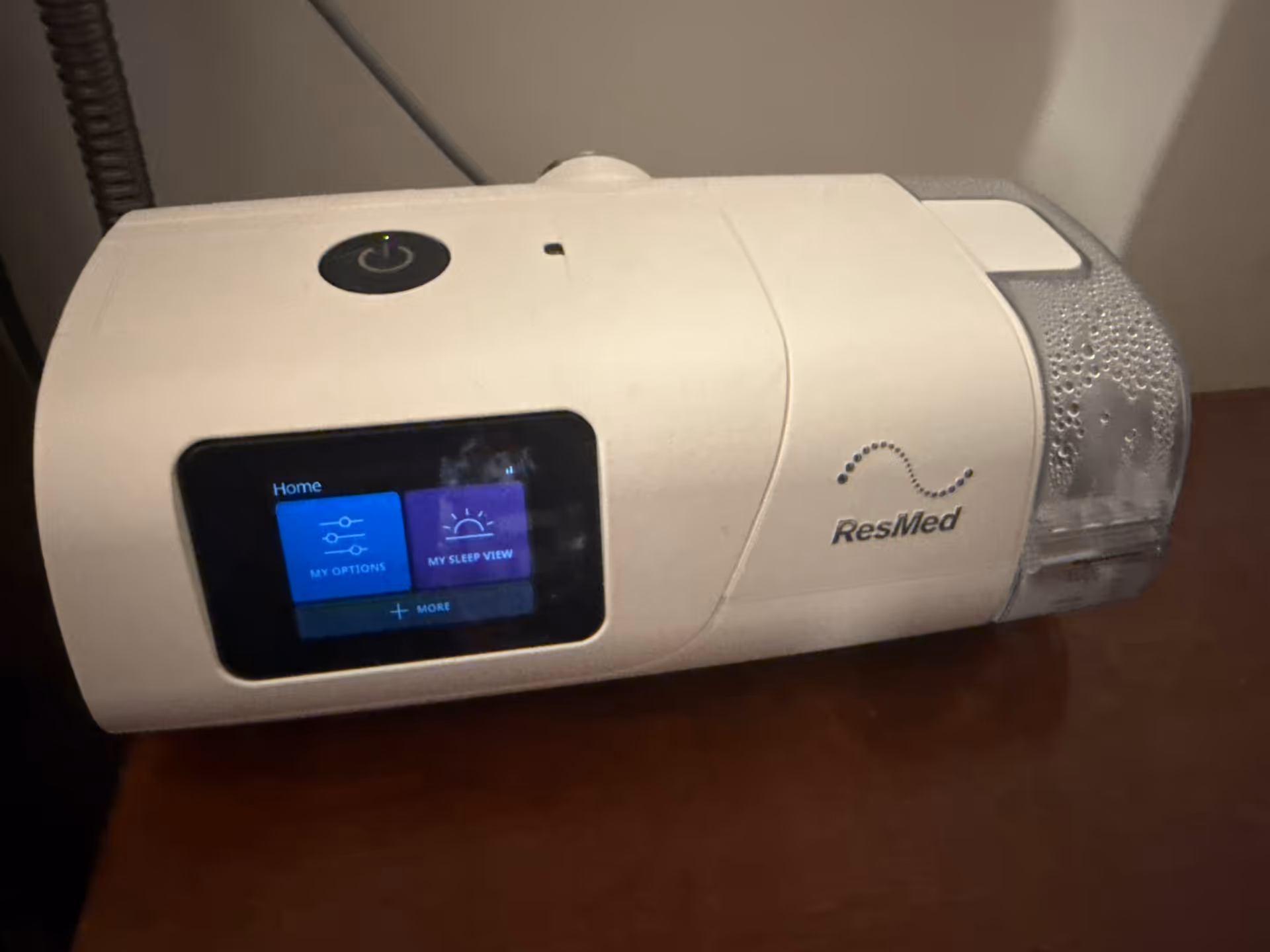 Close-up of a white ResMed CPAP device with a displayed home screen.