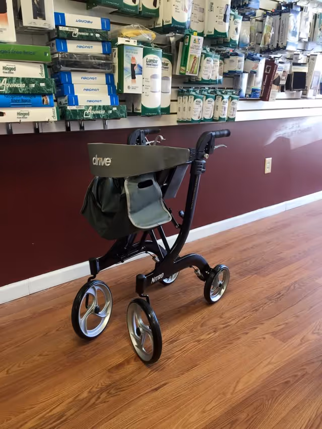 A four-wheeled walker on a wood floor beside shelves of medical supplies in a facility.