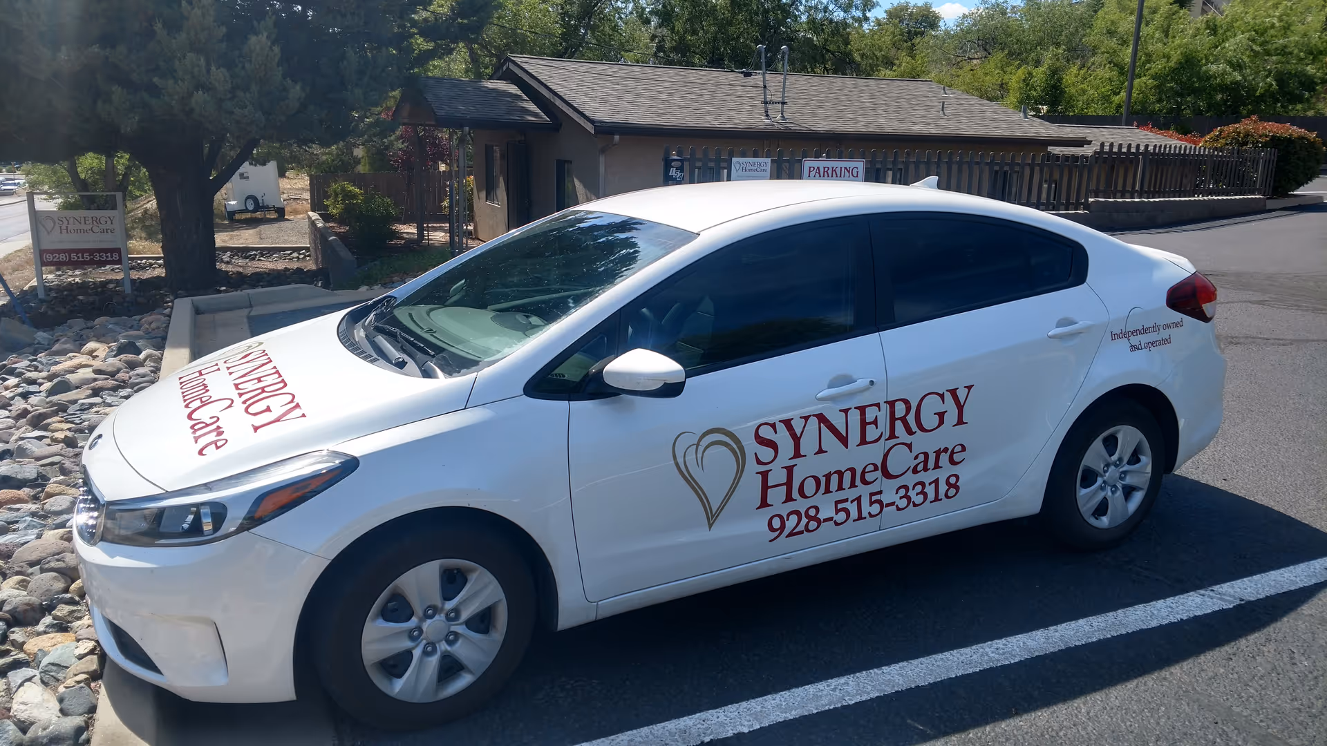 White SYNERGY HomeCare car parked in a lot beside a small building.
