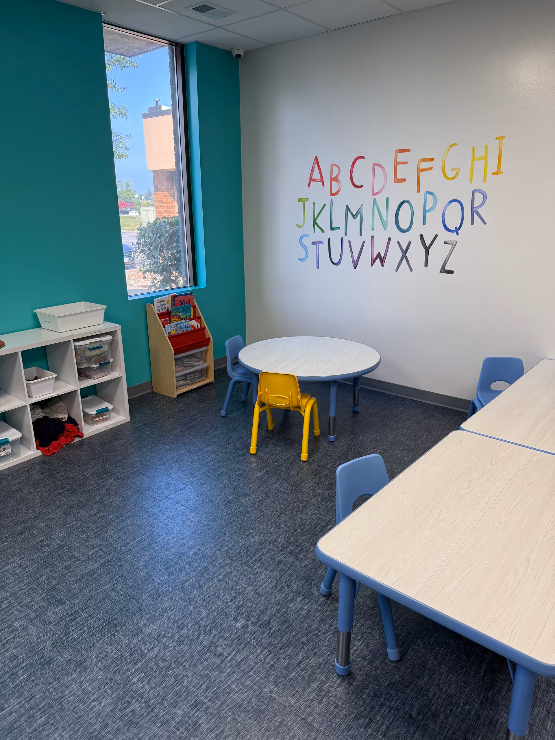 Colorful therapy room with alphabet mural, round table, and small chairs.