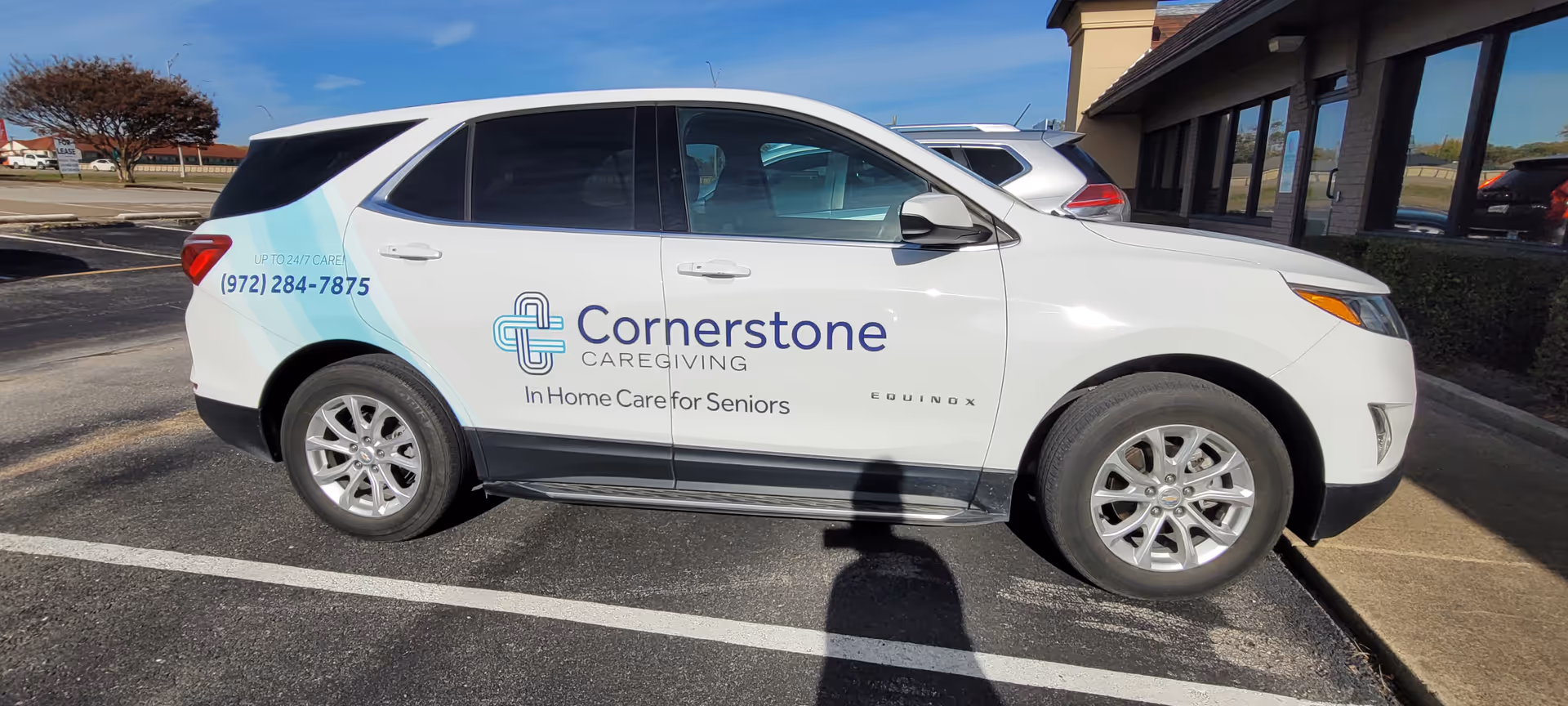 White Cornerstone Caregiving vehicle parked in a lot beside building.