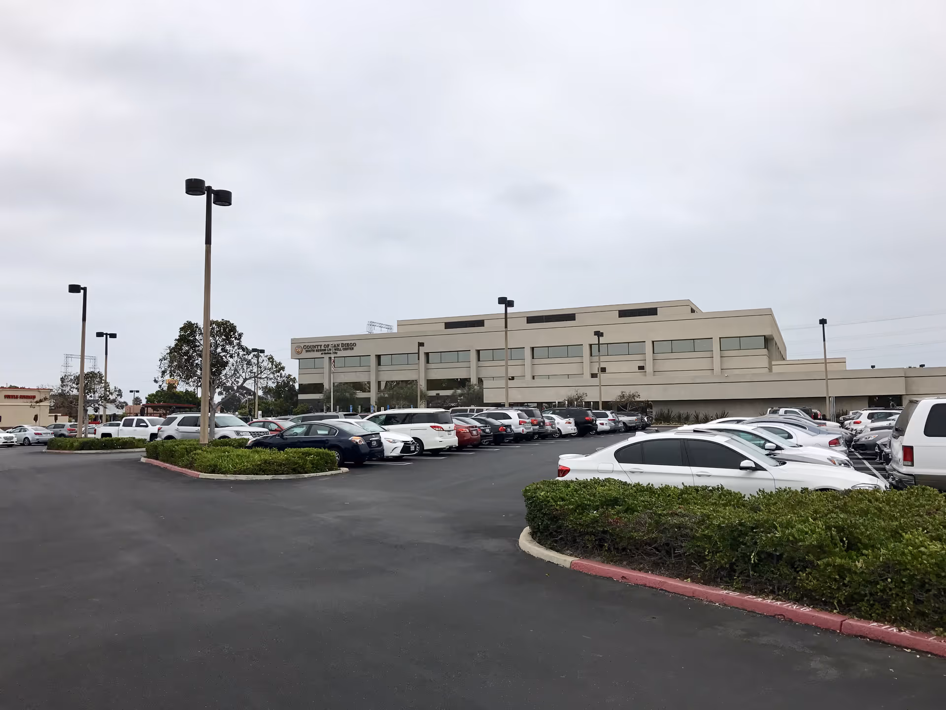 Exterior view of a beige San Diego IHSS Public Authority building with a large parking lot.