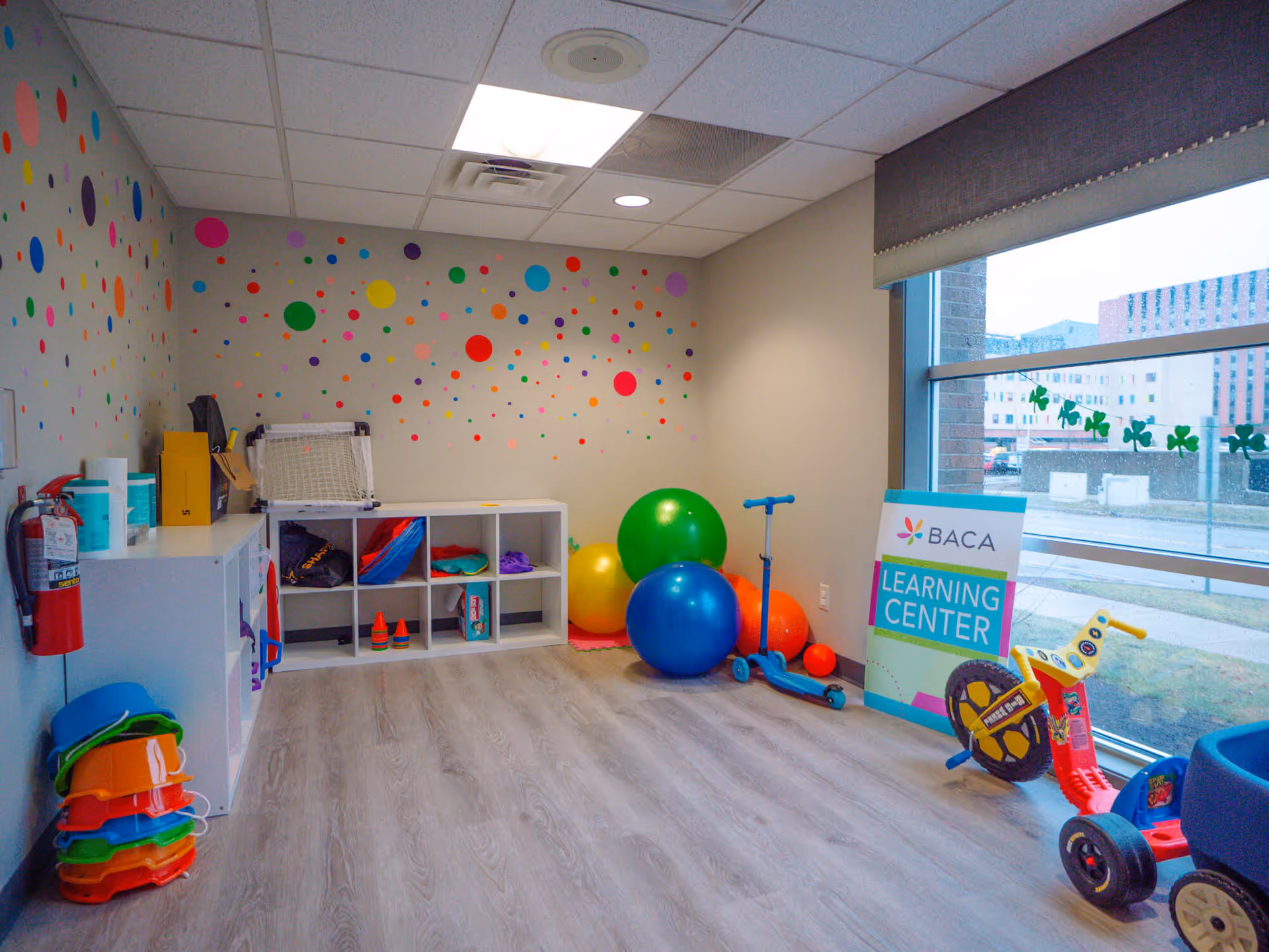 Bright playroom at BACA Learning Center with colorful wall dots, shelves, and toys.
