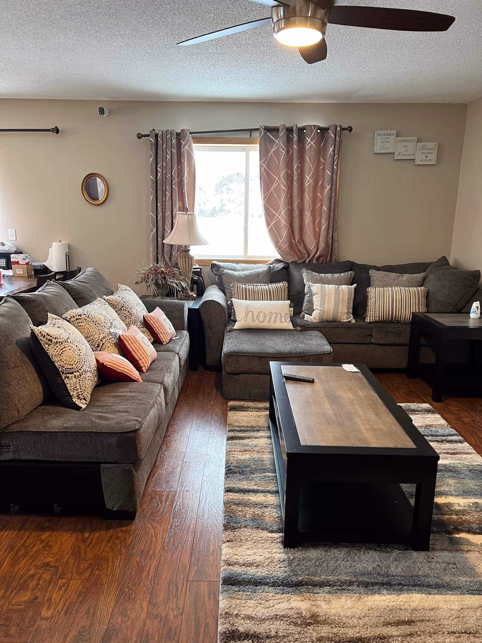Cozy living room with gray sectional sofas, decorative pillows, curtains, a coffee table, and a window.