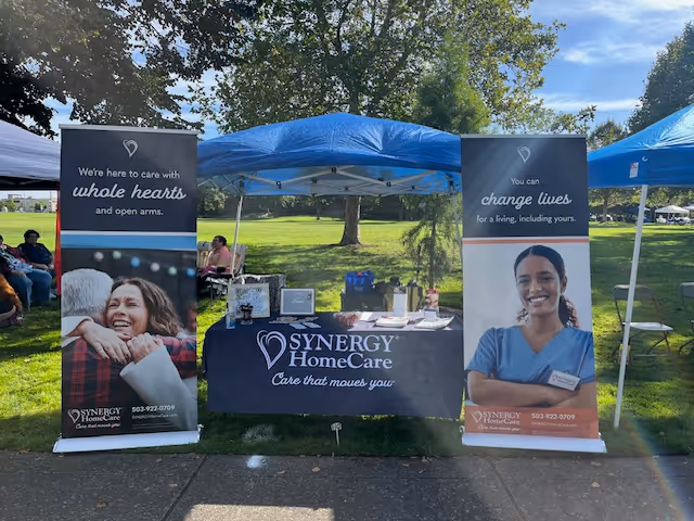 Outdoor care fair setup with blue tents, banners featuring Synergy HomeCare, and a registration table.
