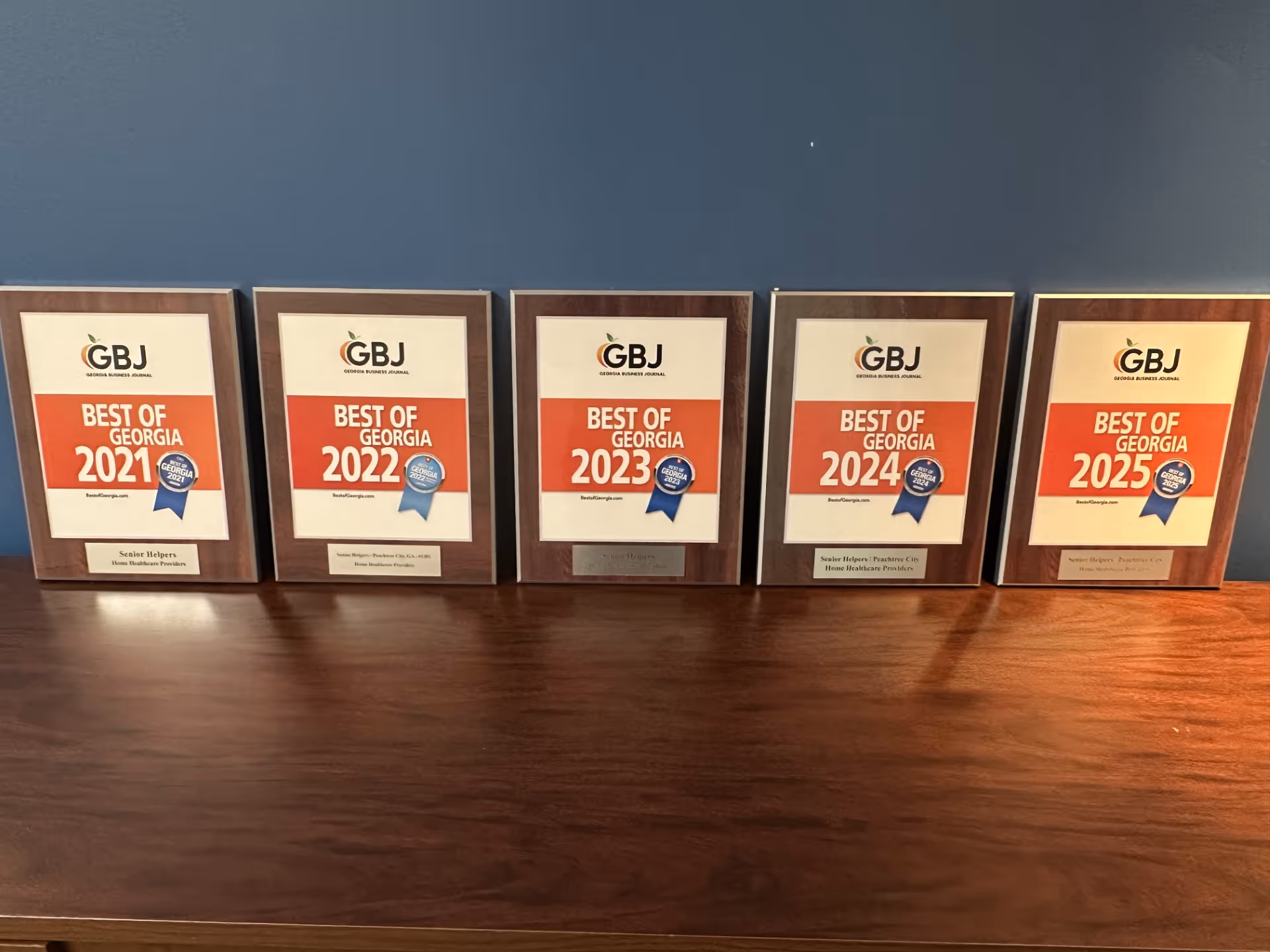 Row of Senior Helpers plaques titled Best of Georgia on a dark wood shelf.