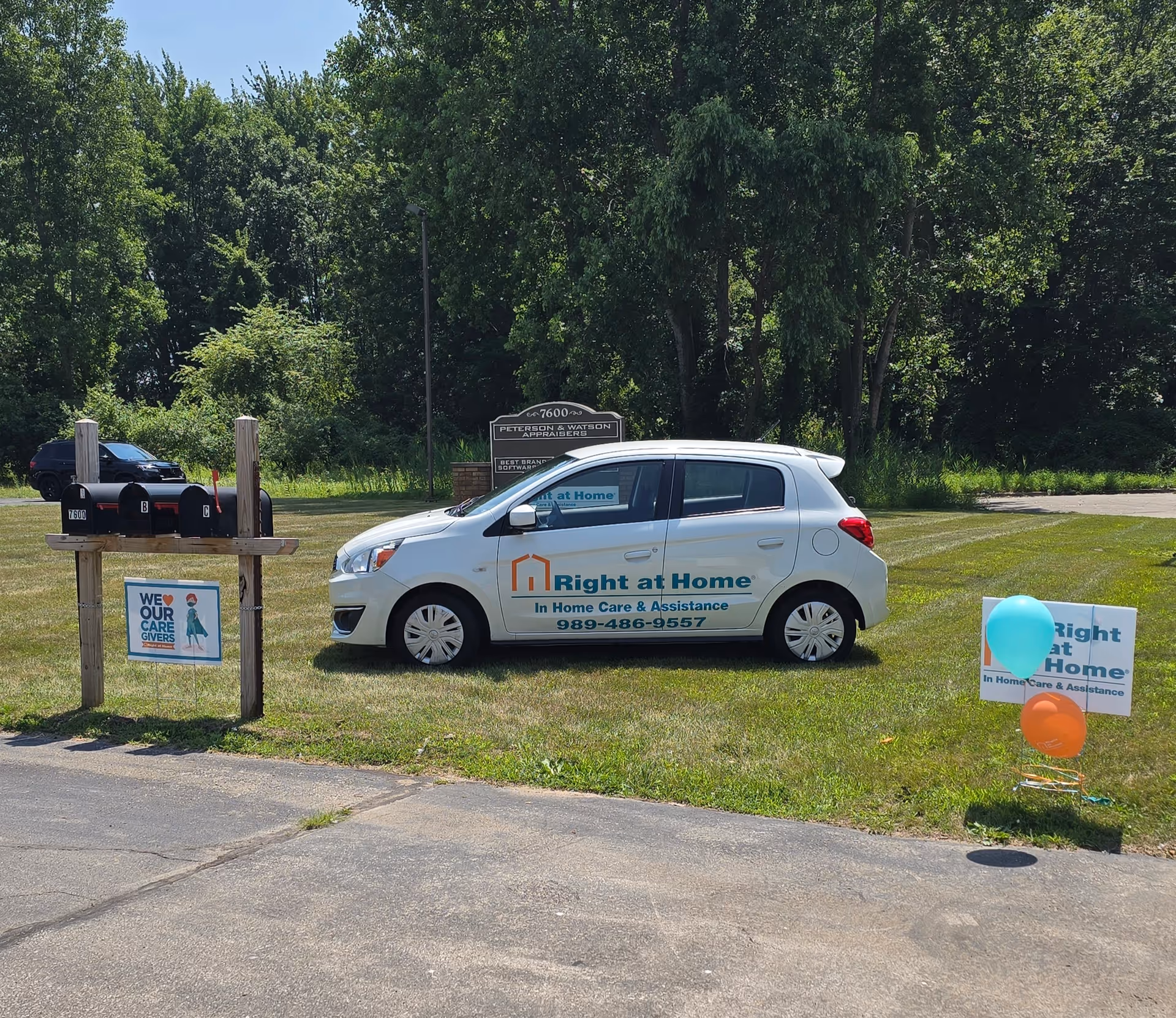 Right at Home care vehicle parked on a grassy roadside with signs and balloons.