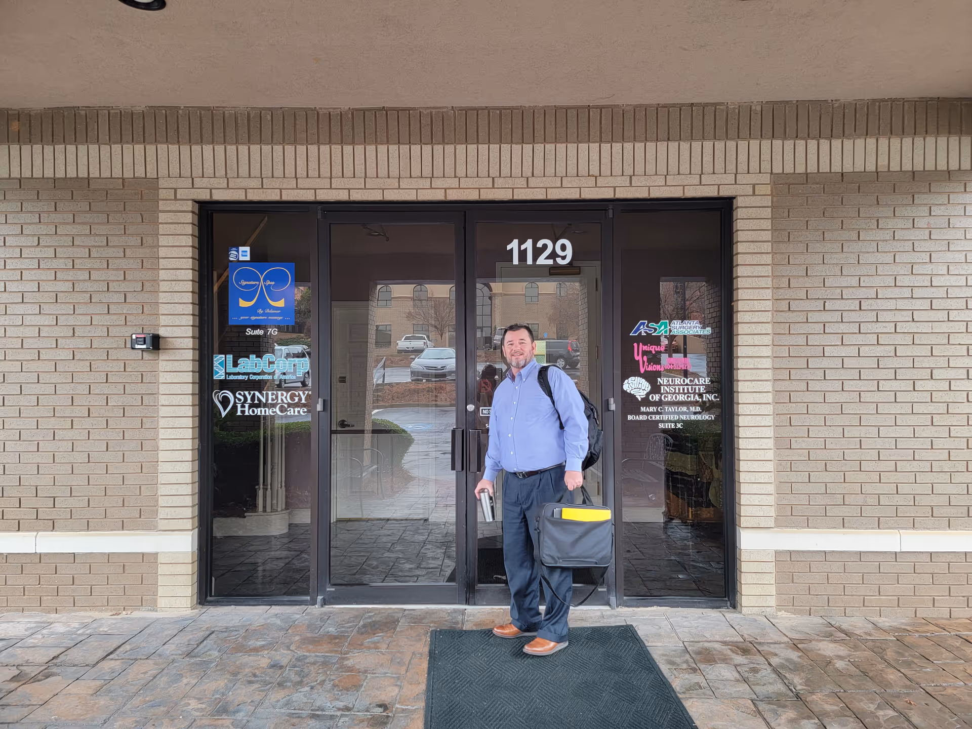 A man stands at the glass entrance of a Synergy HomeCare facility.