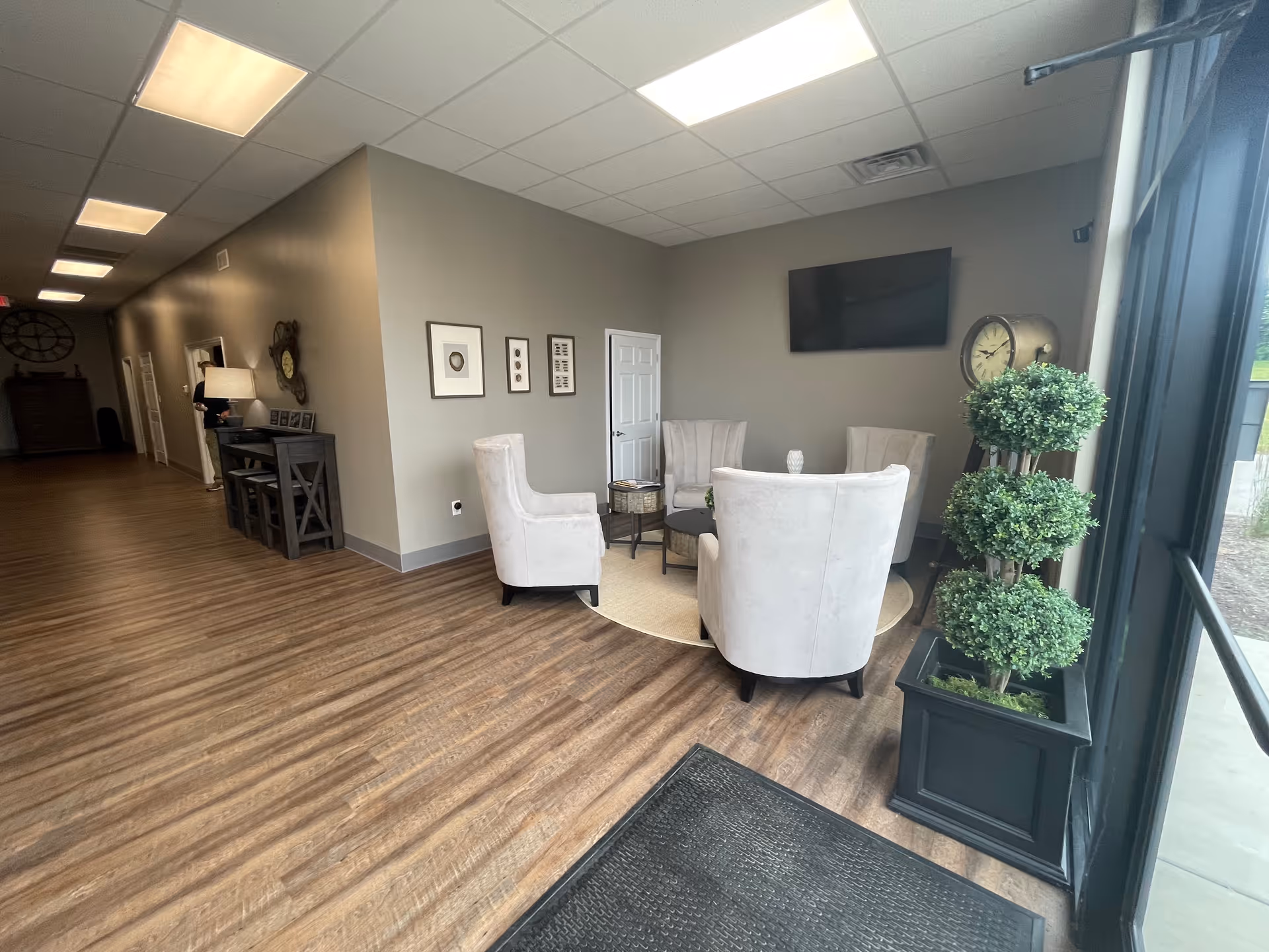 Natural light fills a cozy lounge with beige chairs and a windowed entry.