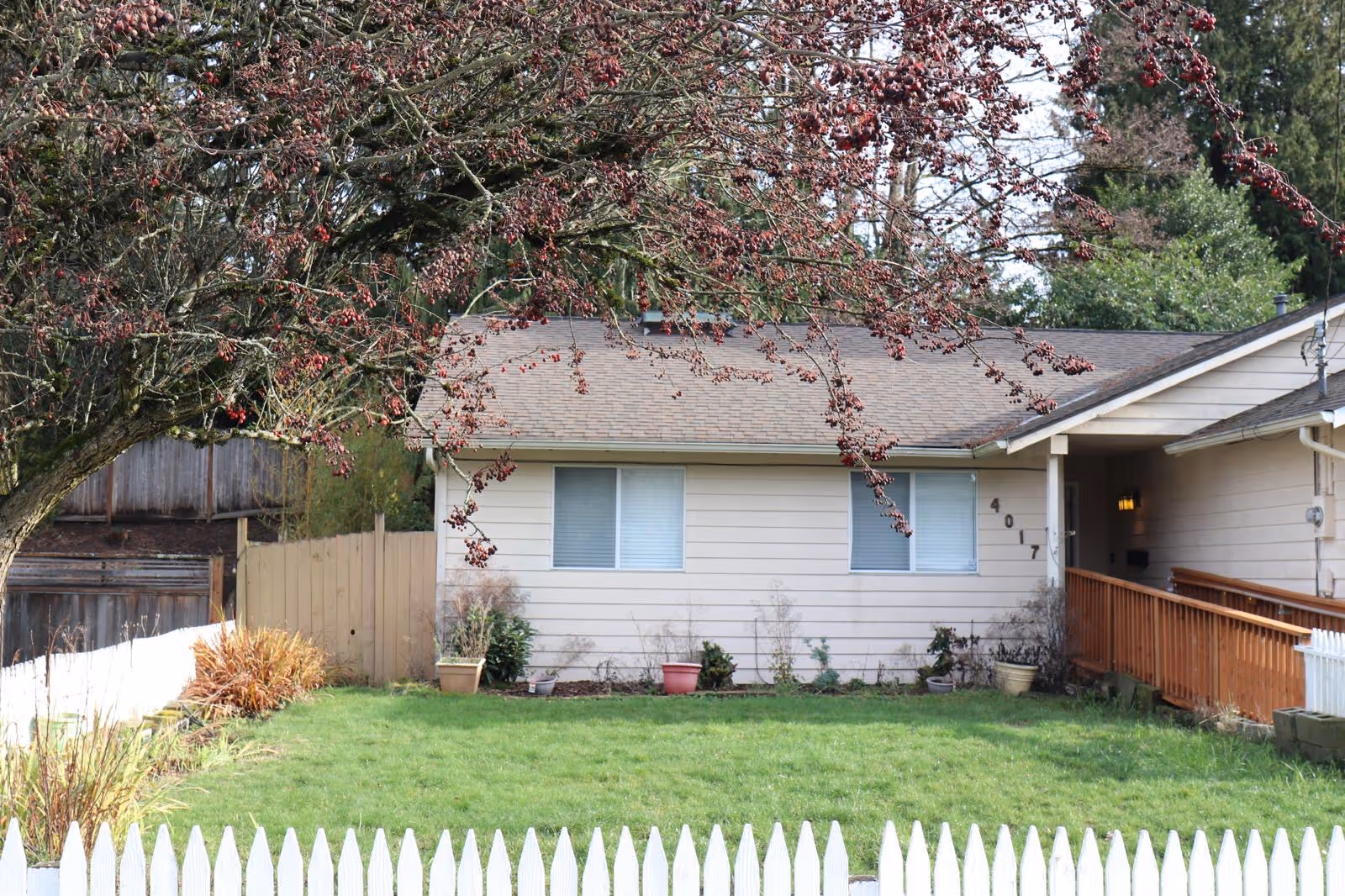 Front view of a single-story beige adult family home with ramp, lawn, and white fence.