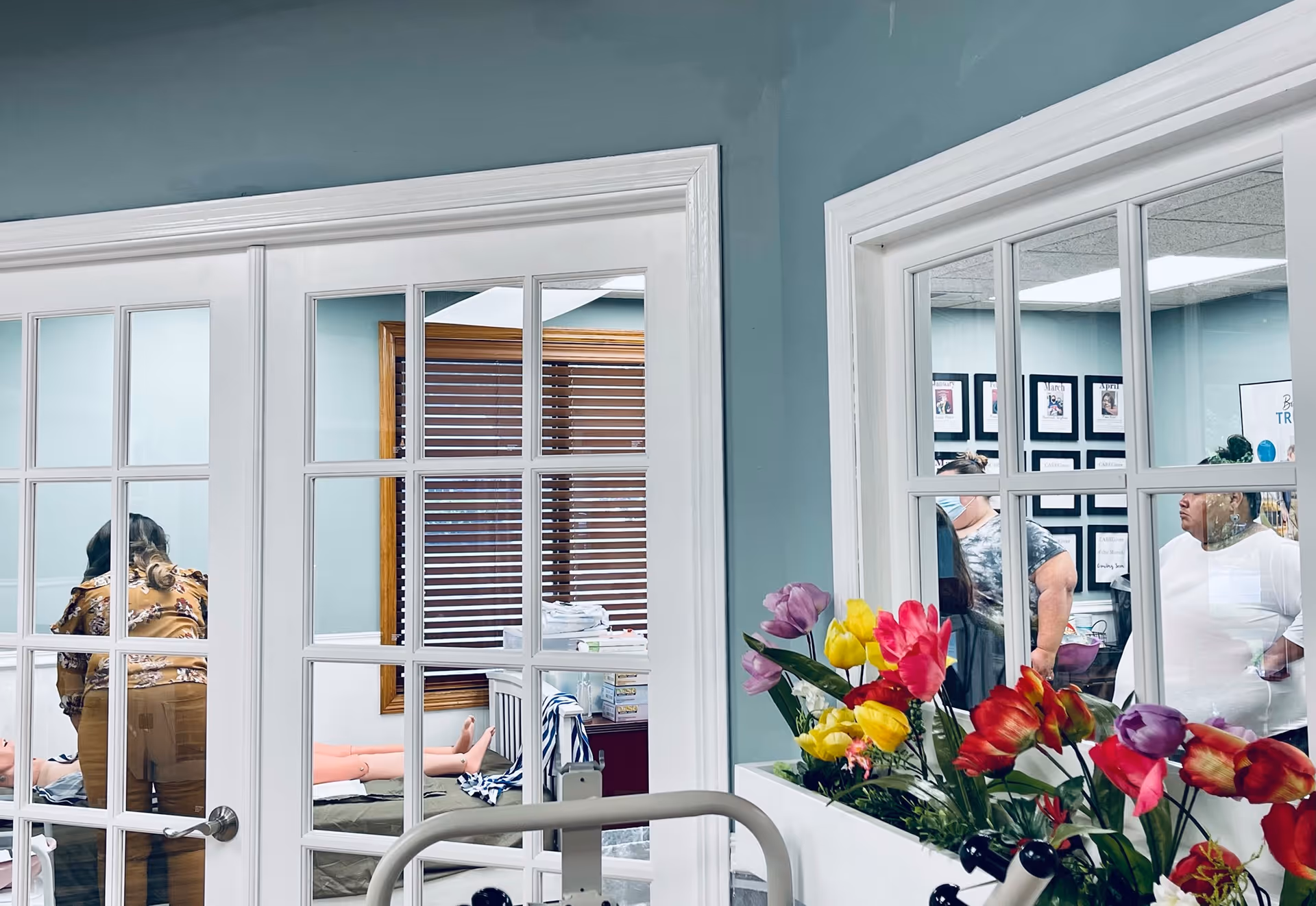 Interior facility scene with glass doors, colorful flowers, and staff or residents visible.