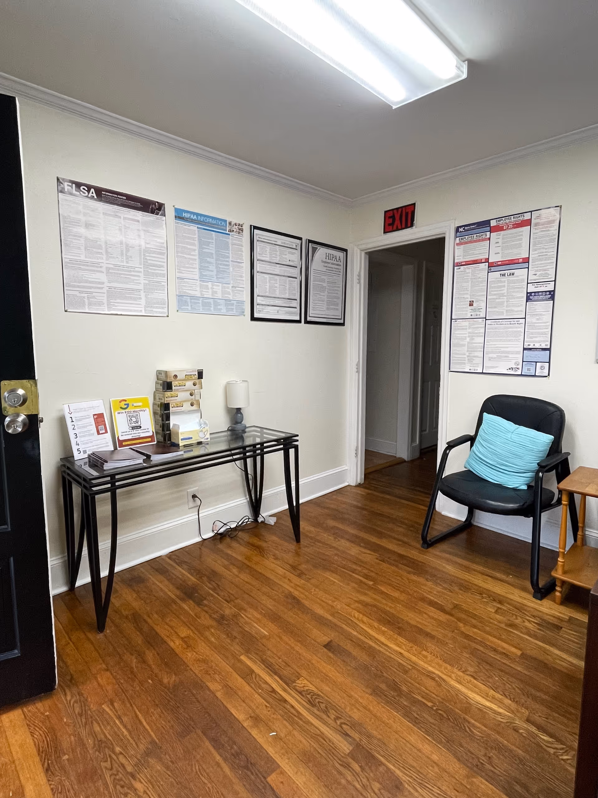 Small interior lobby with a glass-top table, chair, and wall-mounted posters.