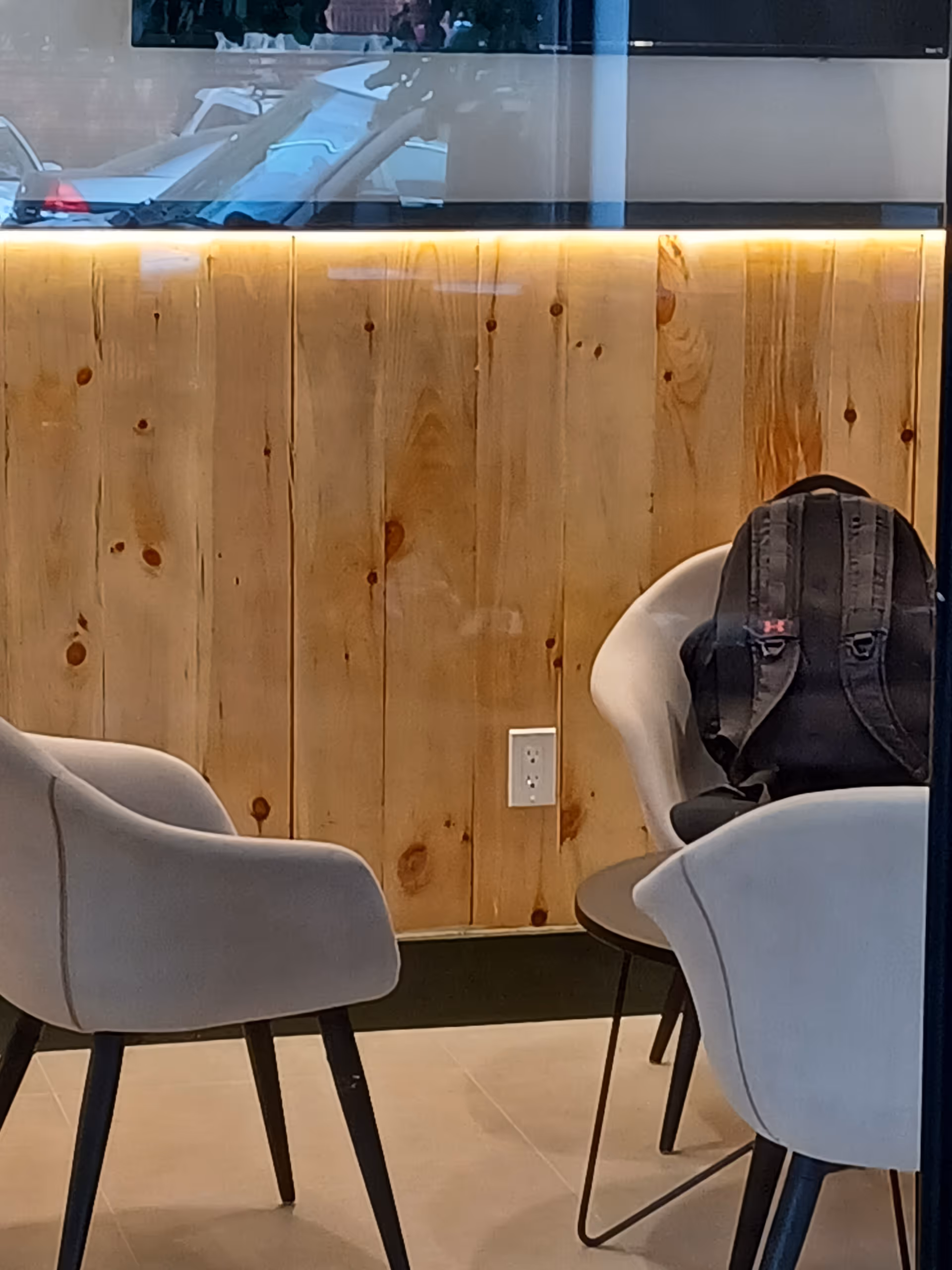 Interior seating area with light chairs and a wooden paneled wall, backpack resting on chair.