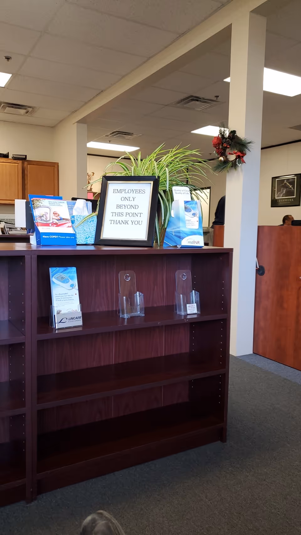 Reception area with dark wood shelving, a plant, and an employees-only sign.