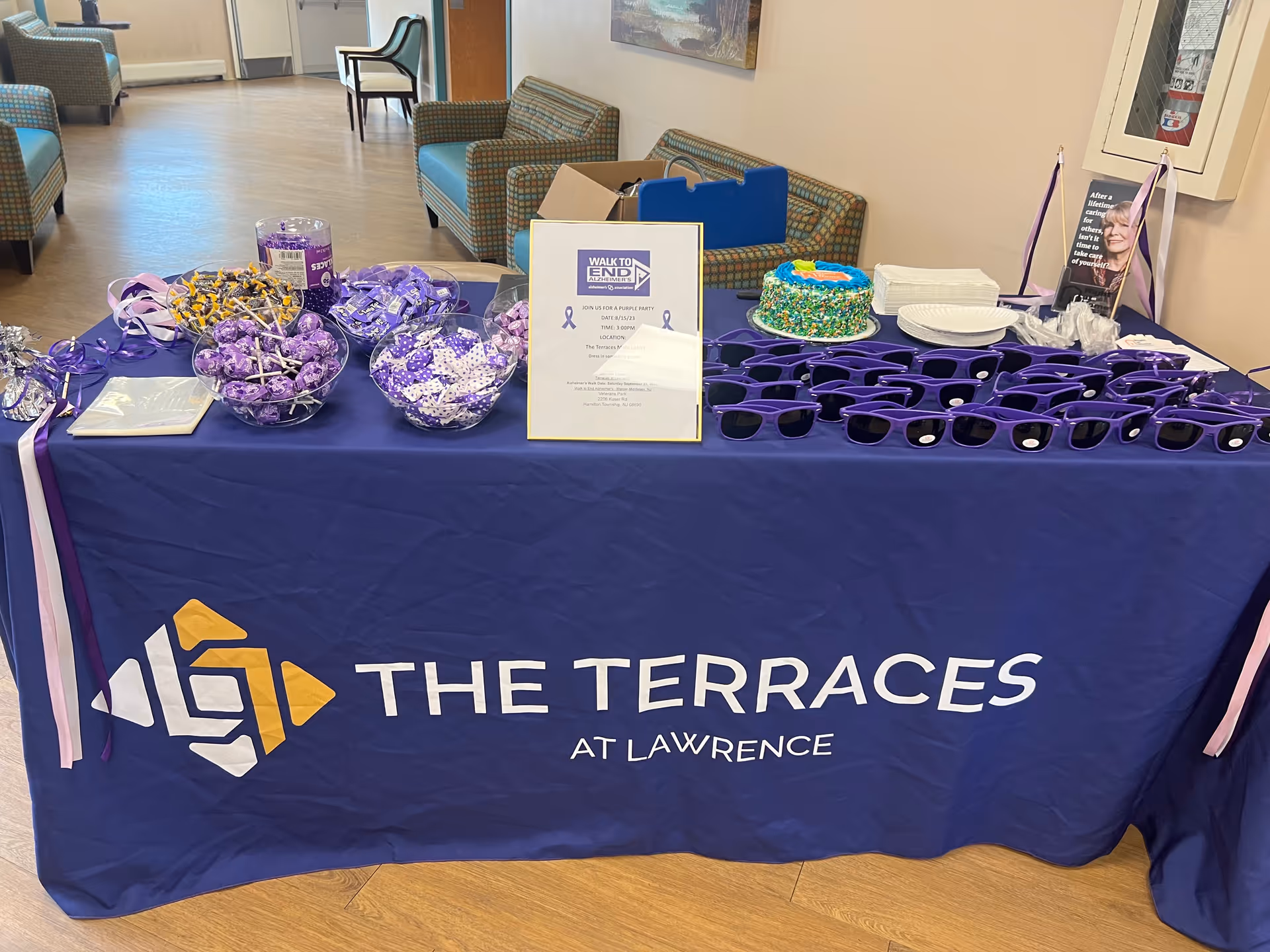 A long table draped in purple at a lobby lounge with decor and cake.
