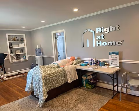A furnished care room with a bed, desk, and Right at Home logo on the wall.