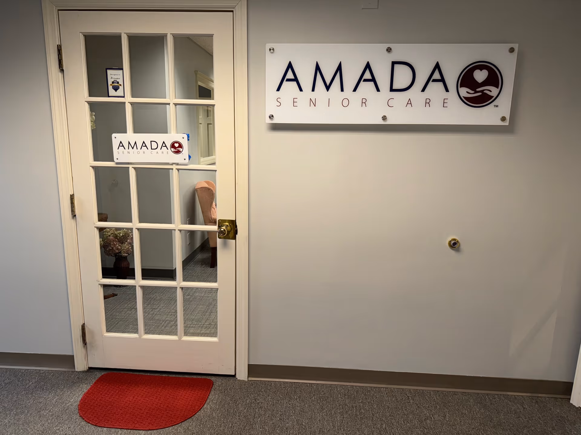 Interior hallway with glass-paneled door and Amada Senior Care sign.
