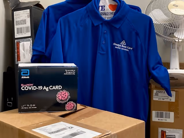 Blue Always Best Care polo shirt displayed beside a COVID-19 Ag Card box on a desk.
