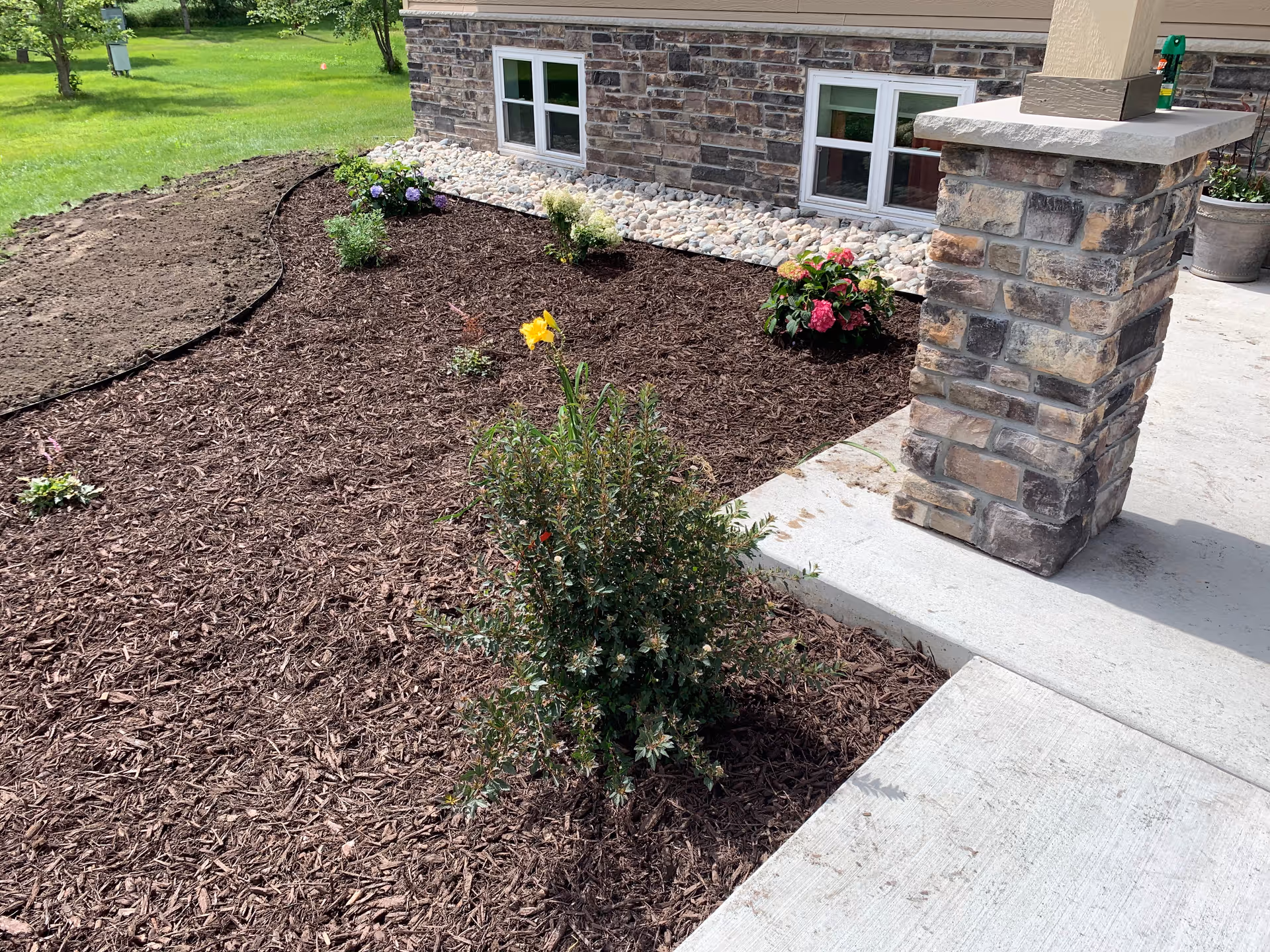 Mulched garden beds, stone pillar, and walkway at Harmony Home Health Care entrance.