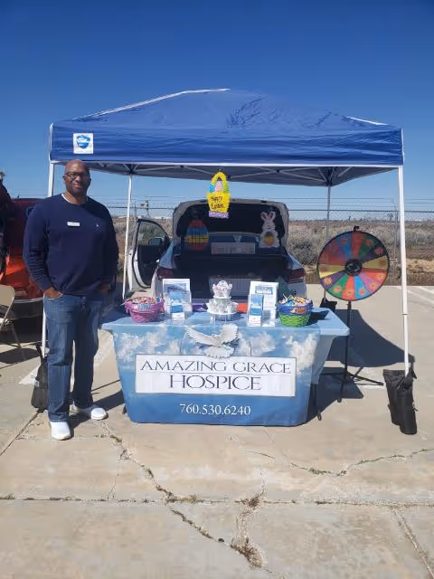 Man stands beside a blue canopy booth displaying Amazing Grace Hospice outdoors.