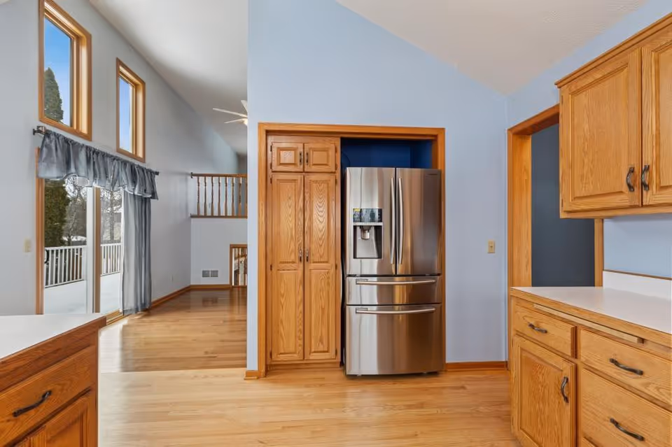 Bright kitchen with wooden cabinets, stainless steel refrigerator, and light blue walls.