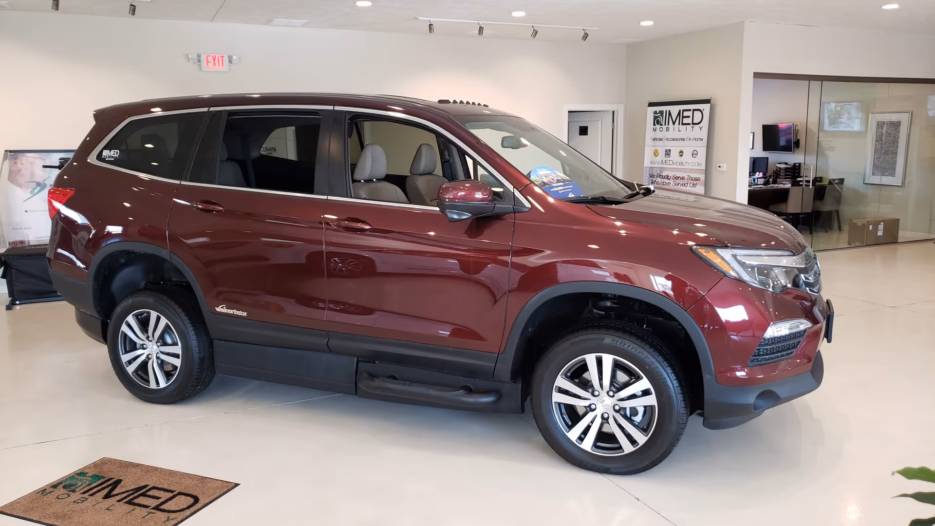 Maroon SUV displayed inside MobilityWorks showroom with office area in background.