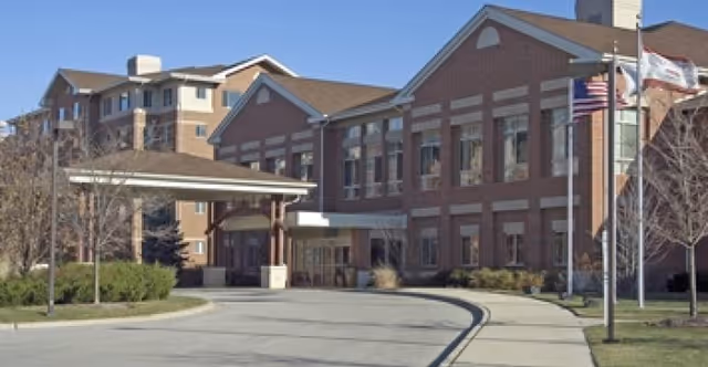 Brick senior living facility exterior with entrance canopy and flagpoles along a curved driveway.