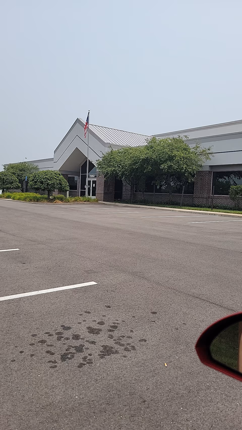 Front exterior of a facility with entrance, flagpole, trees, and a parking lot.