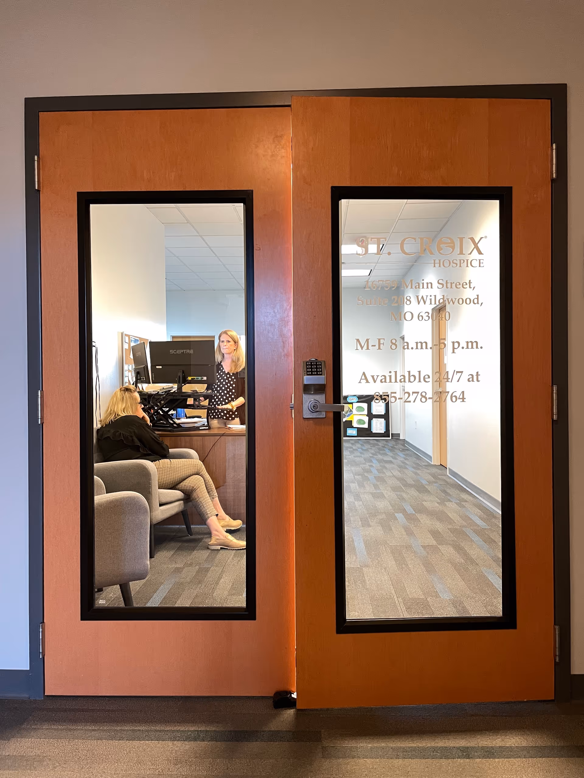 Double wooden doors with glass panels reveal a reception area and staff.