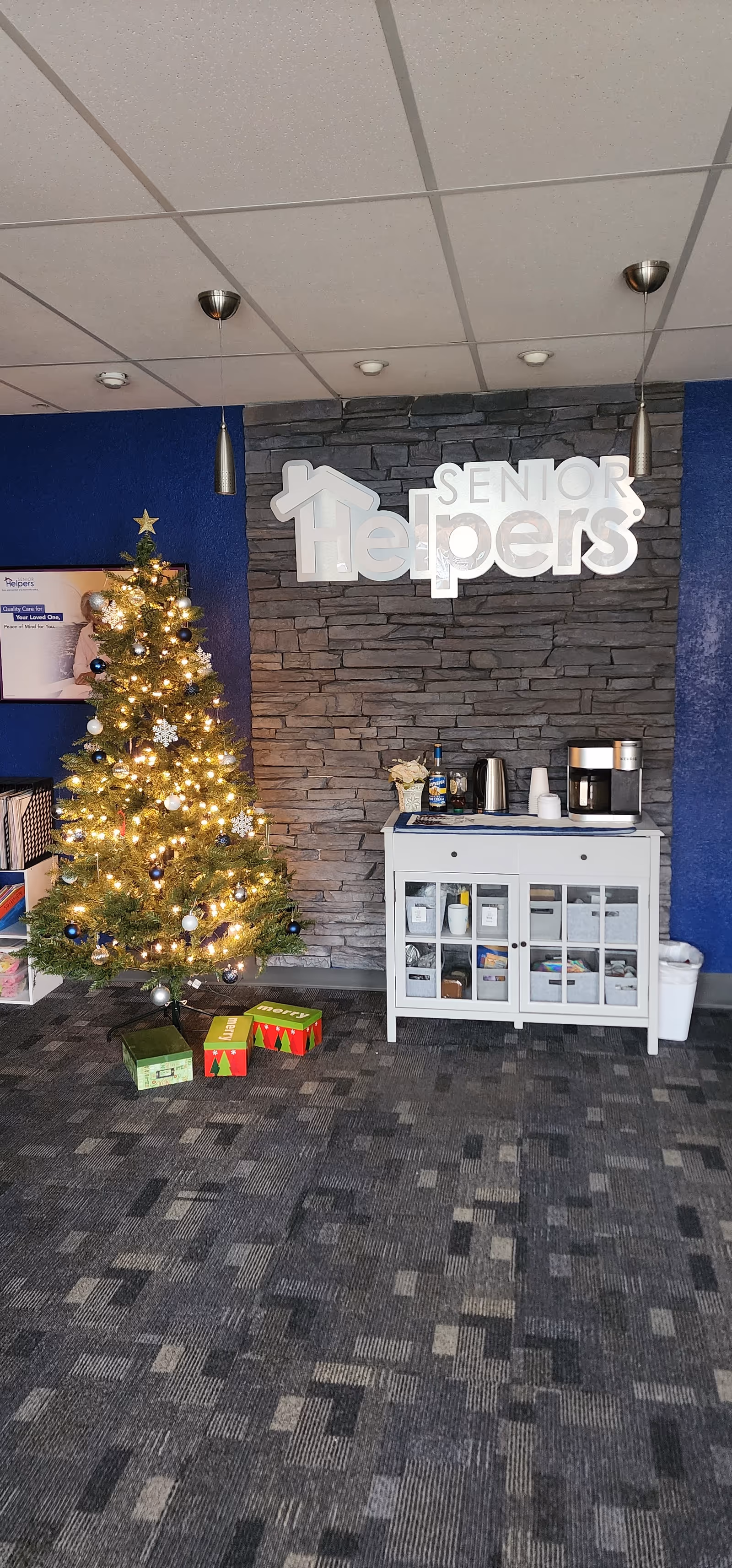 Interior lobby with Christmas tree, gifts, and a Senior Helpers sign on a stone wall.