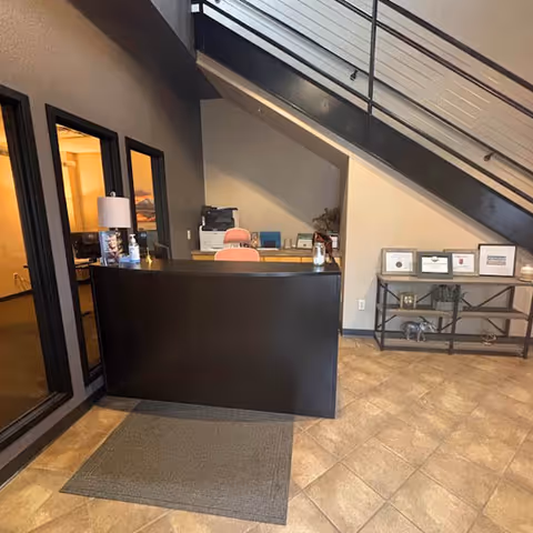 Reception desk beneath a staircase in a modern senior living facility lobby.