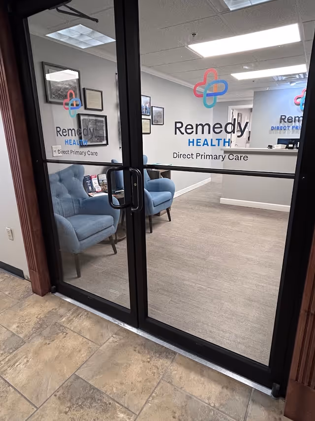 Glass doors into a Remedy Health Direct Primary Care reception area with blue chairs and art.