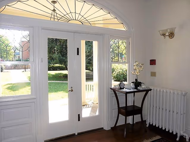 Bright white entryway with double doors, arched transom window, and a small table by a radiator.