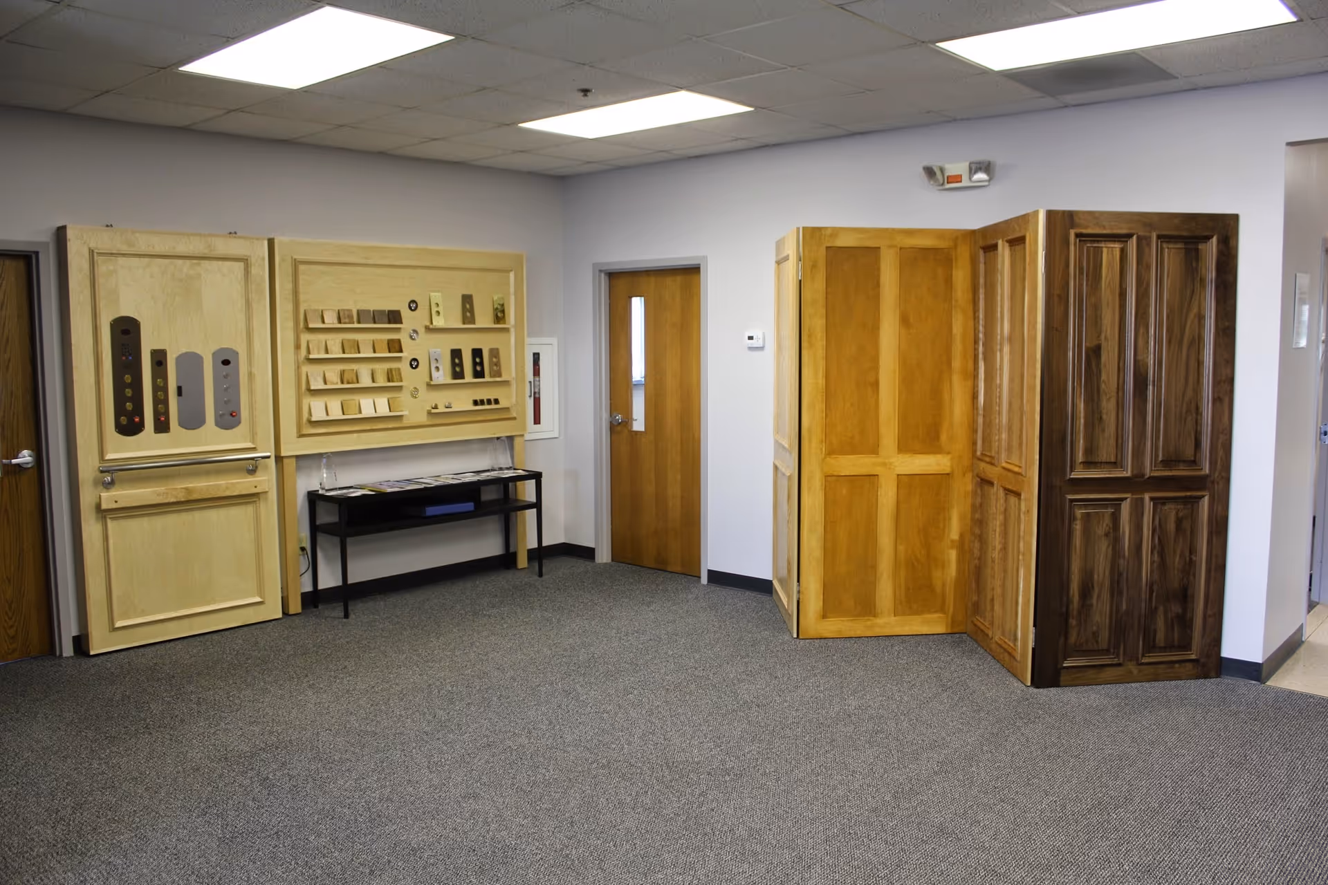 Interior showroom area displaying wooden doors, sample boards, and a carpeted floor.
