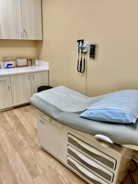 Medical examination room with an adjustable chair, cabinets, and wall-mounted stethoscope.