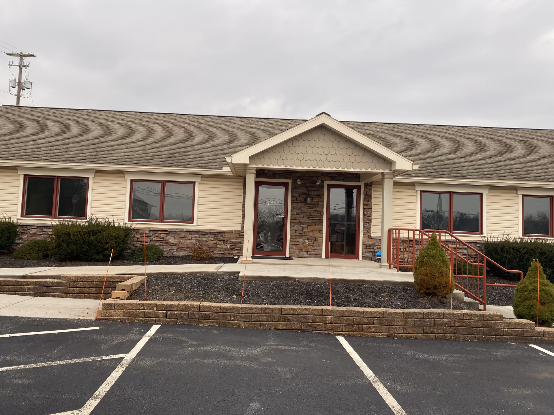 Front view of a single-story SYNERGY HomeCare facility with brick entrance and parking area.