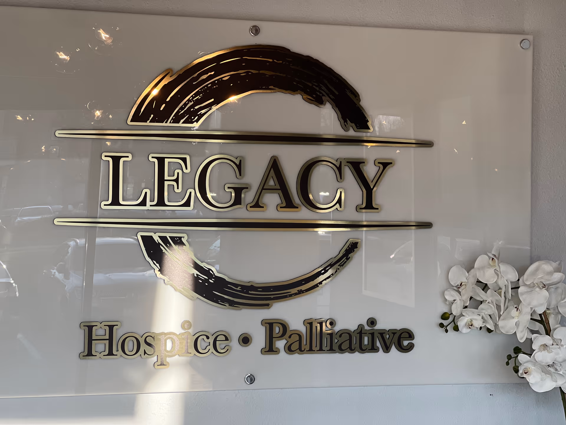 Interior wall sign displays Legacy Hospice and Palliative Care with a curved logo and orchids.