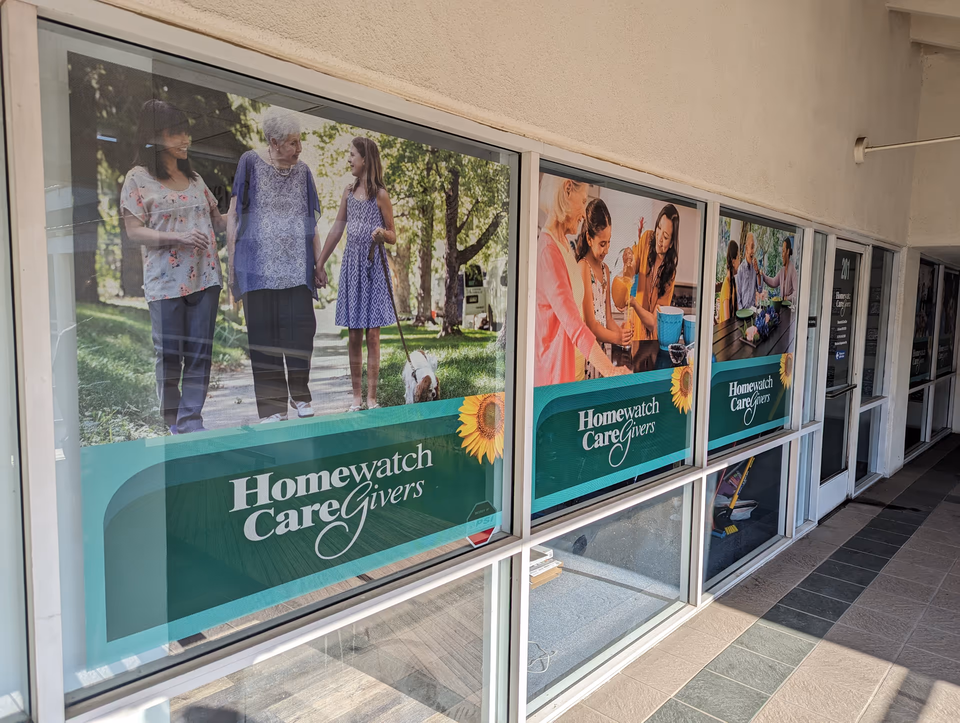 Storefront windows display Homewatch CareGivers posters featuring seniors and caregivers in a park-like scene.