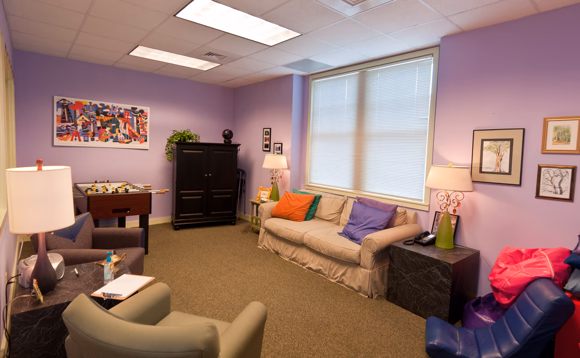 Cozy purple-walled living room with sofa, lamps, artwork, and a foosball table.