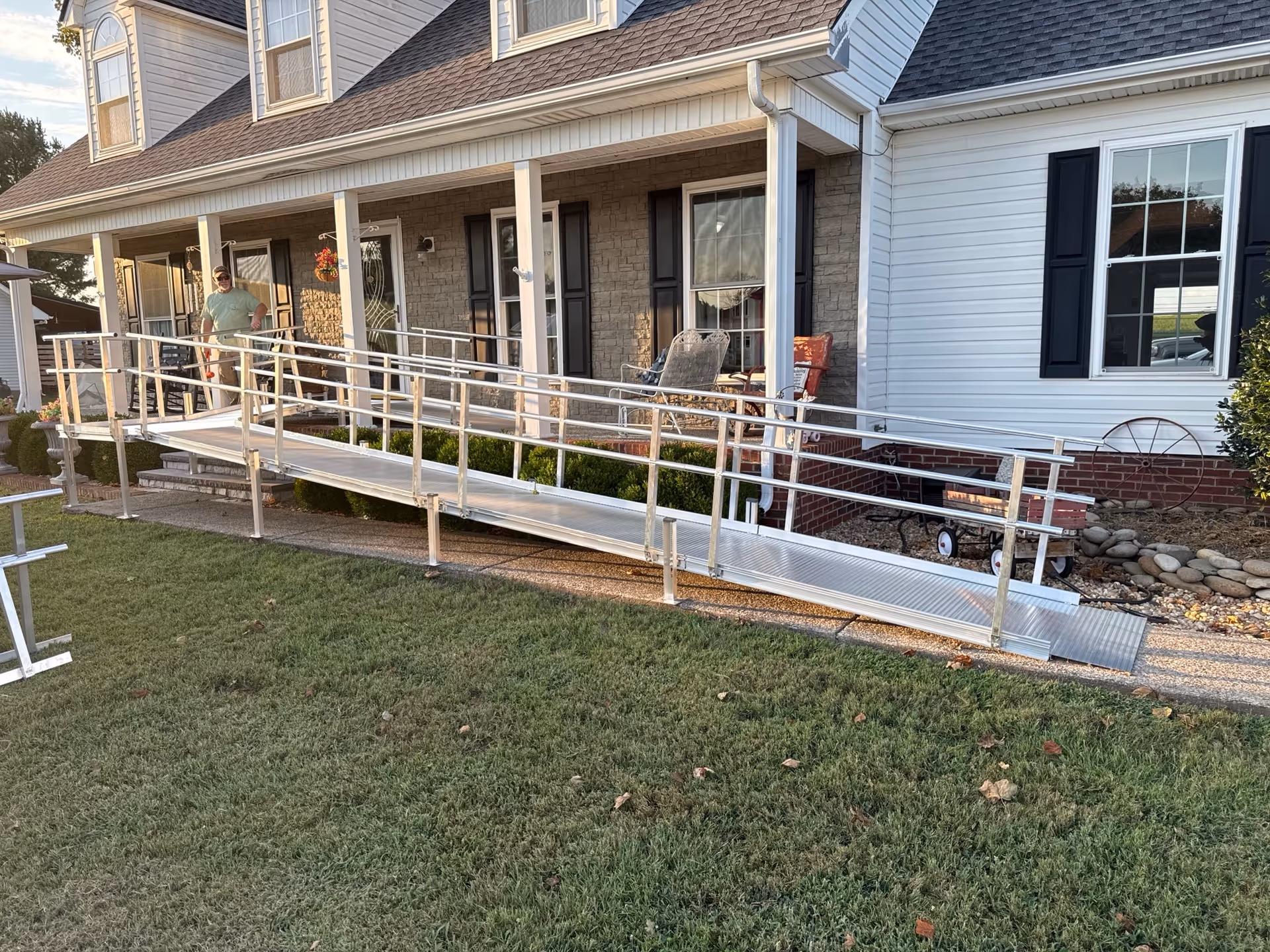 Front view of a house with a metal wheelchair ramp and porch seating.