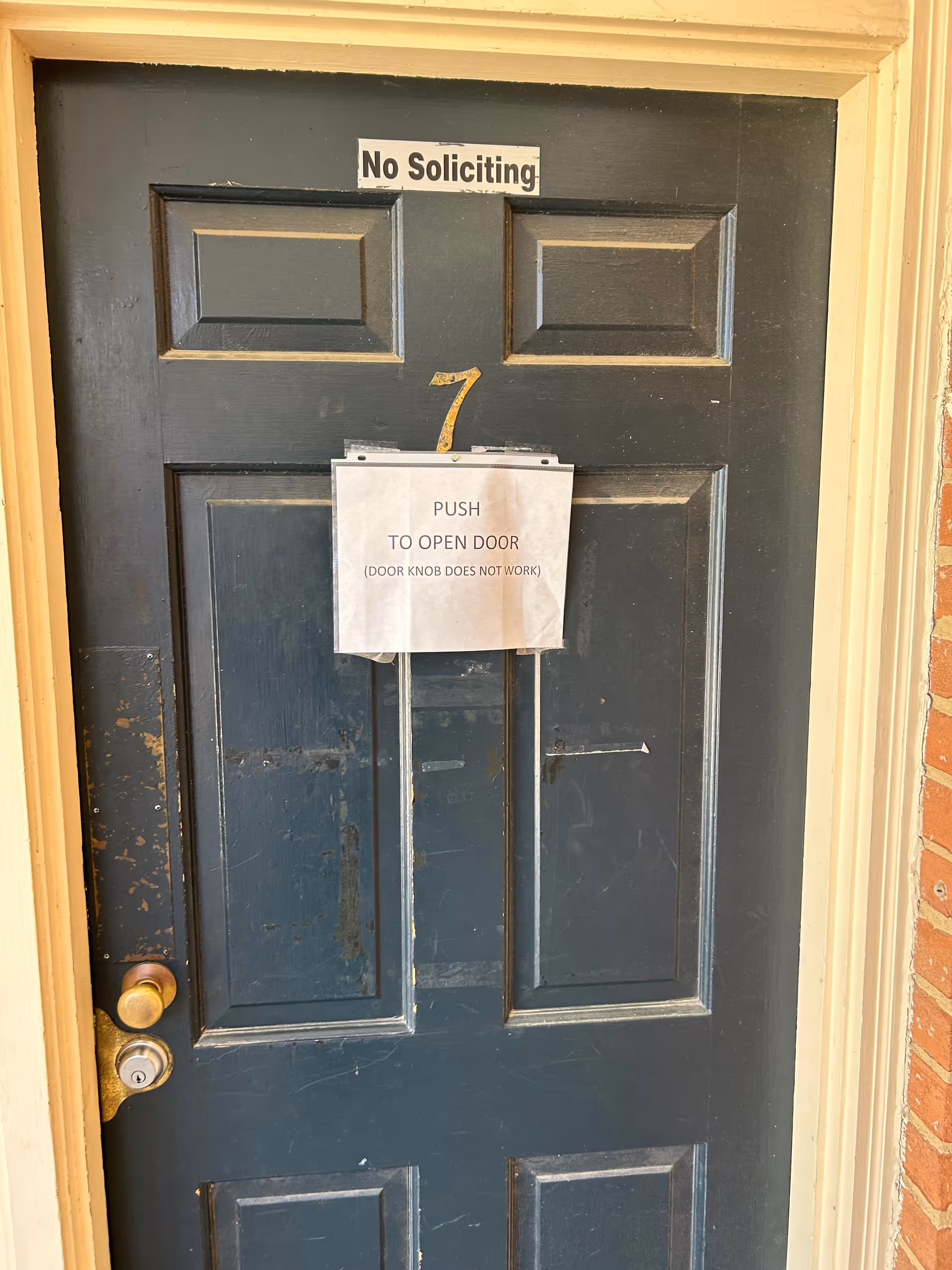 A blue front door with a No Soliciting sign and taped push-to-open notice.