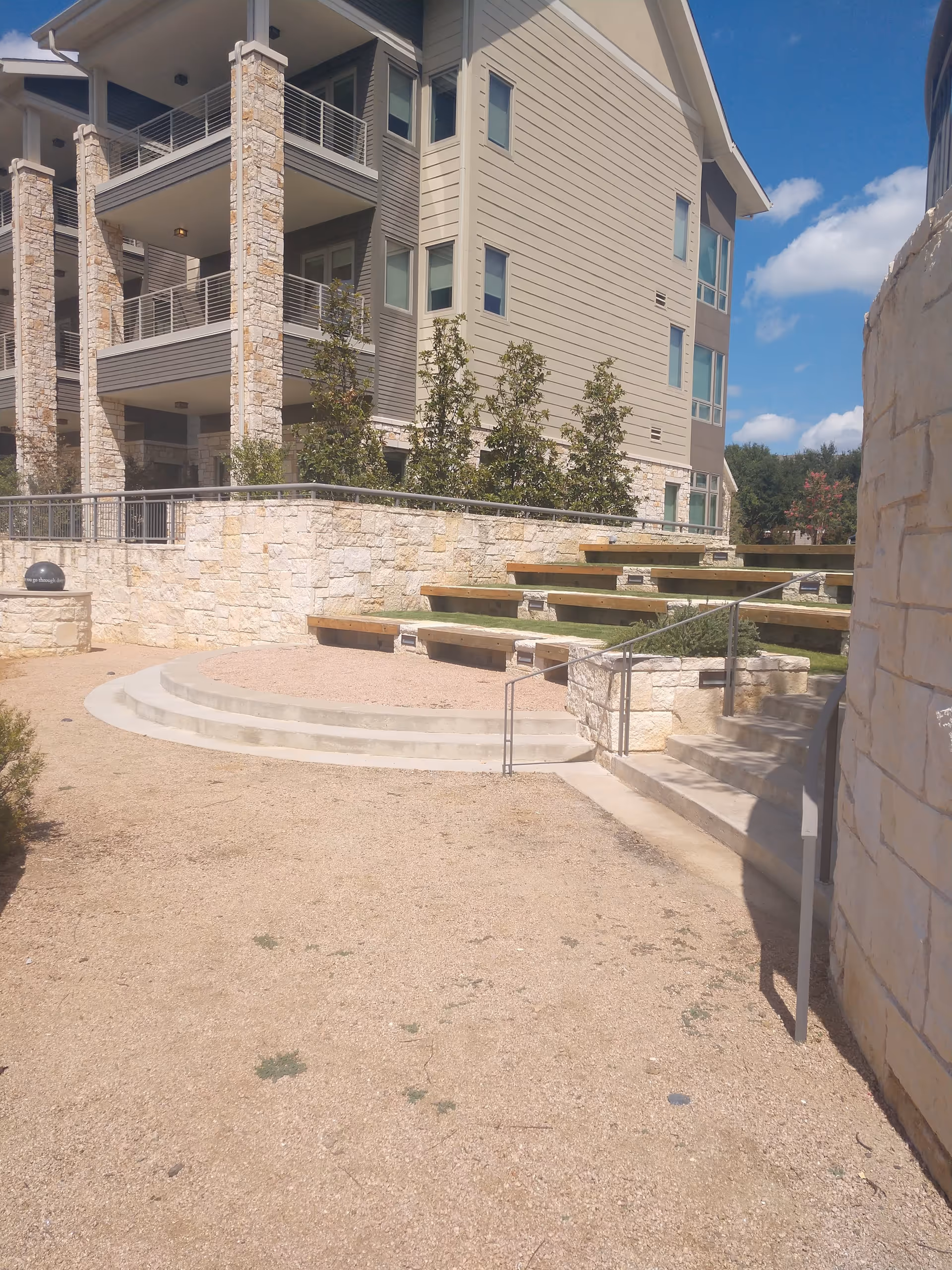 Modern multi-story senior facility exterior with stone walls and tiered outdoor seating.