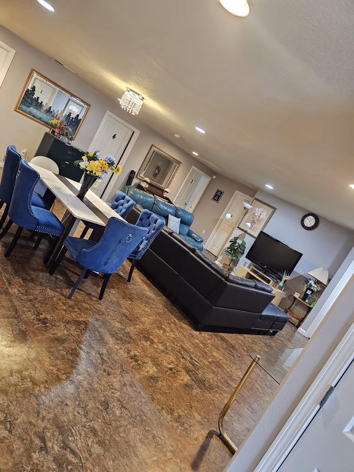 A spacious senior living lounge with blue chairs around a dining table and a black sofa.