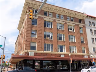 Brick multi-story building with storefronts on the ground floor along a city street.