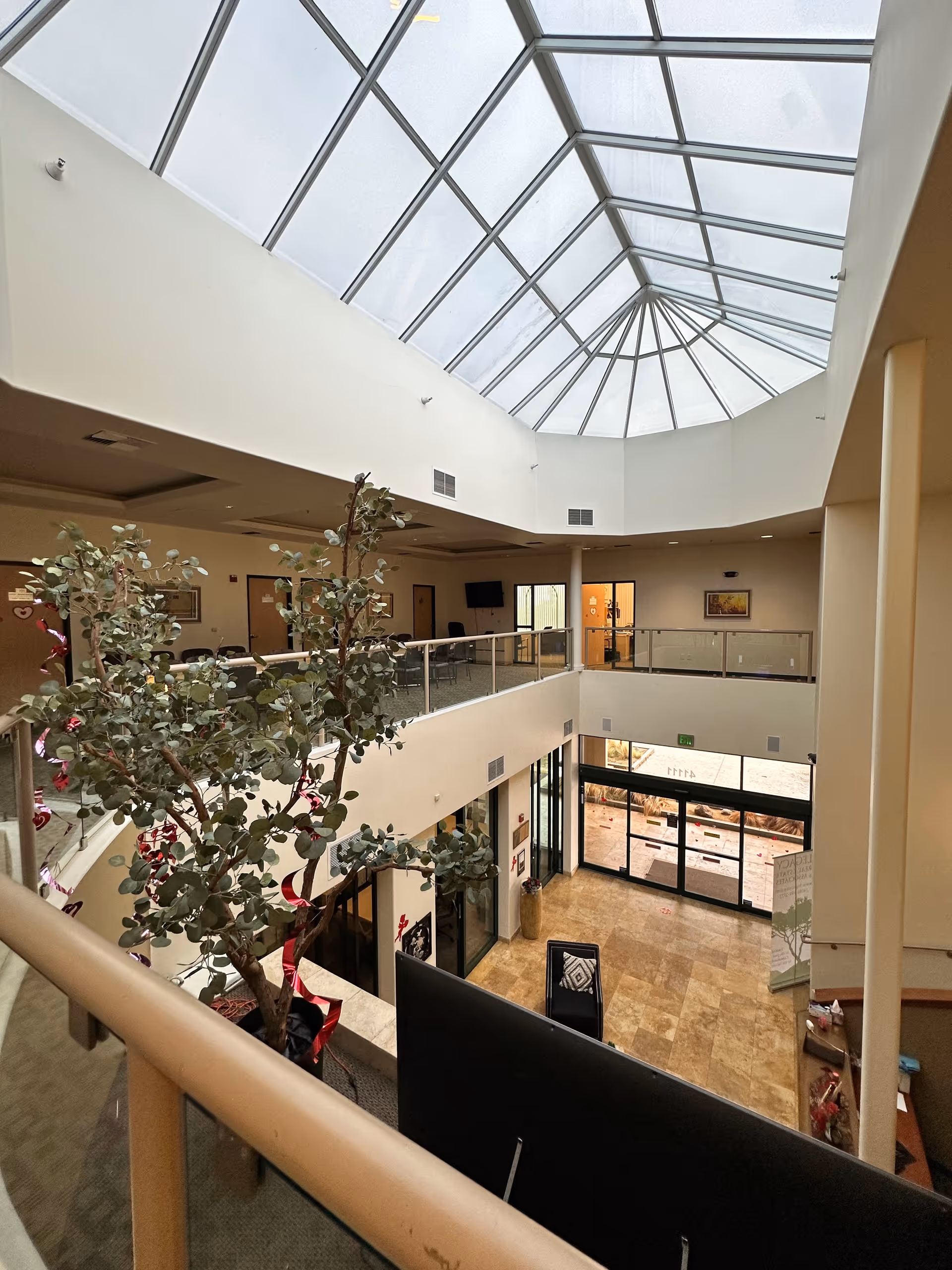 Two-story indoor atrium with glass skylight, railings, and potted tree.
