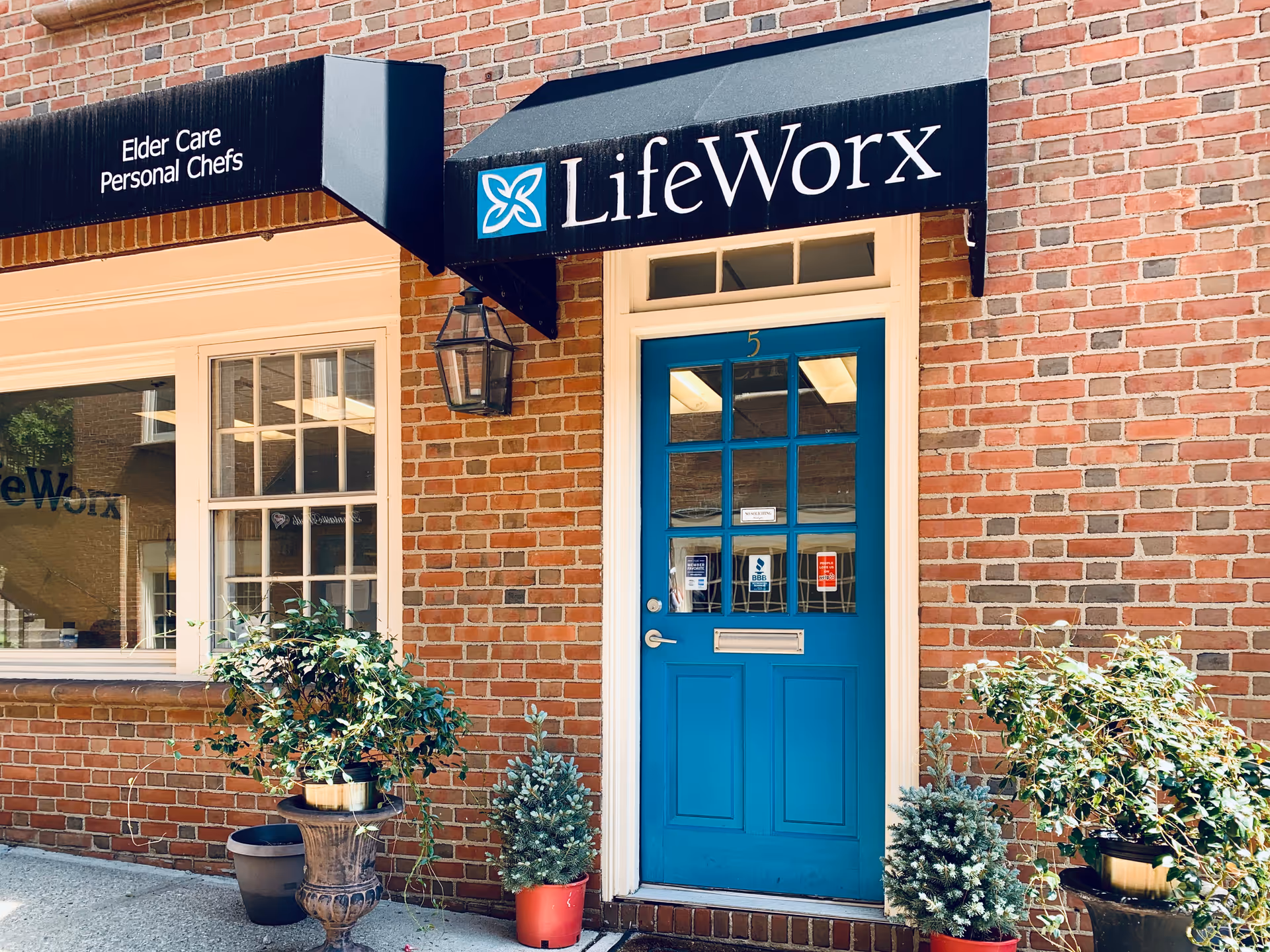 Red-brick building exterior with a bright blue LifeWorx door and potted plants by entrance.